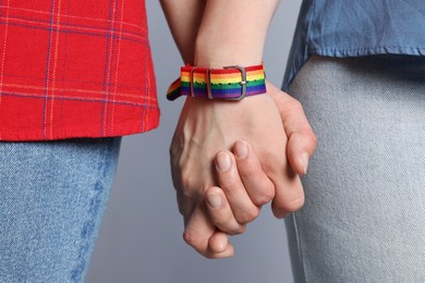 Photo of LGBT concept. Women in rainbow wristbands holding hands on light grey background, closeup