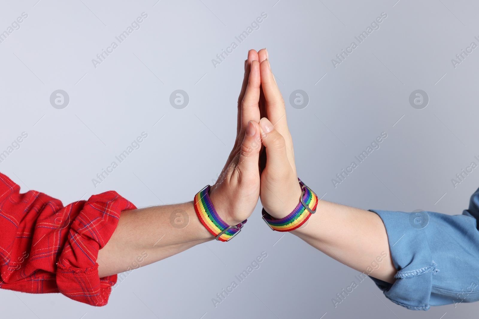 Photo of LGBT concept. Women in rainbow wristbands holding hands on light grey background, closeup
