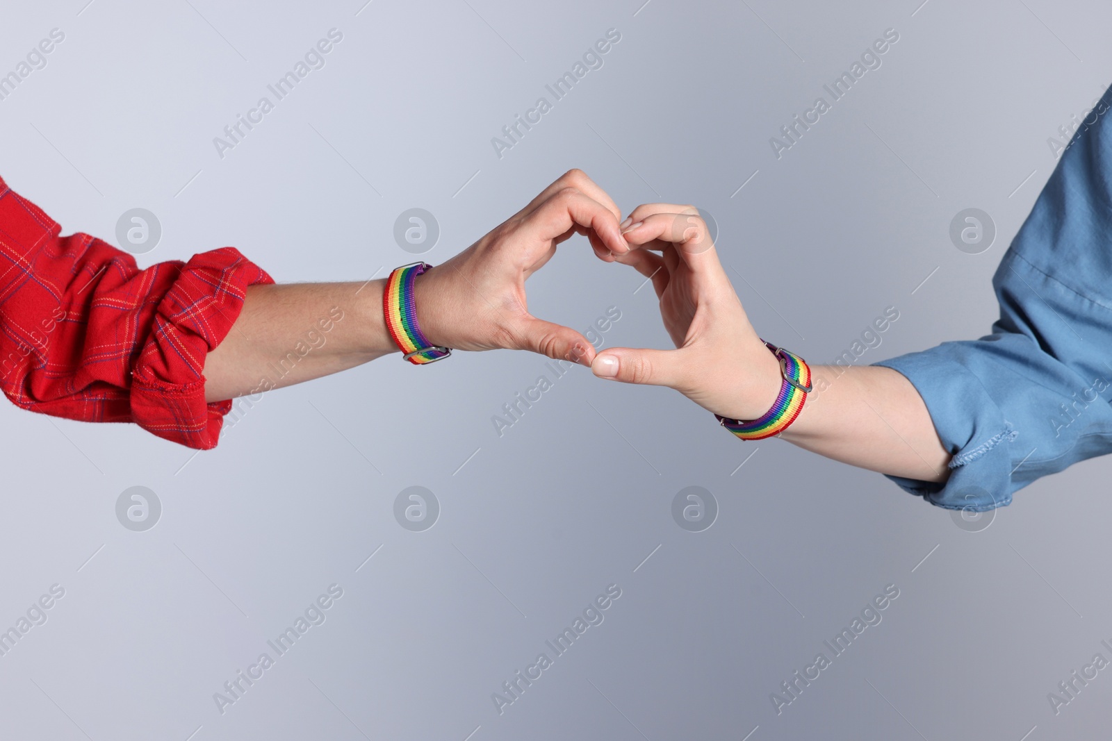 LGBT concept. Women in rainbow wristbands making heart shape on light grey background, closeup Photo of LGBT concept. Women in rainbow wristbands making heart shape on light grey background, closeup