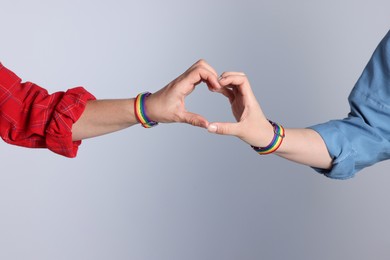Photo of LGBT concept. Women in rainbow wristbands making heart shape on light grey background, closeup