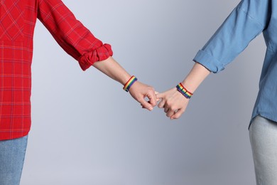 Photo of LGBT concept. Women in rainbow wristbands holding hands on light grey background, closeup