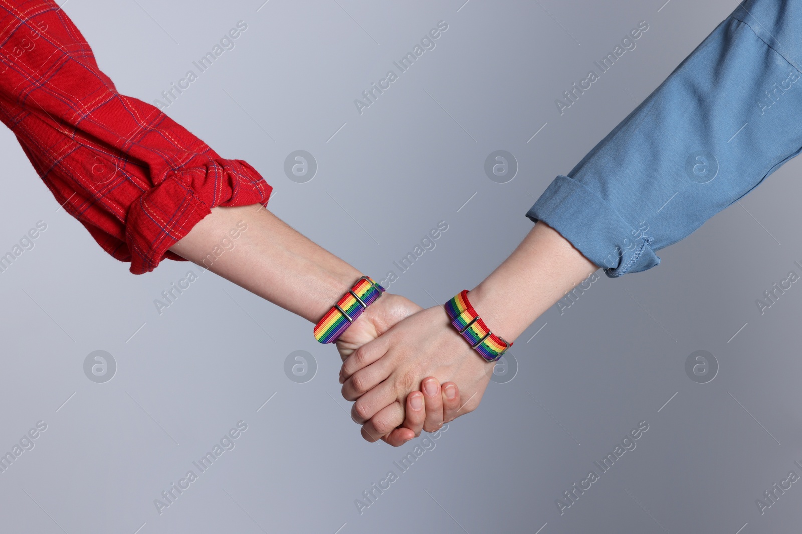 Photo of LGBT concept. Women in rainbow wristbands holding hands on light grey background, closeup