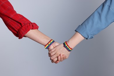Photo of LGBT concept. Women in rainbow wristbands holding hands on light grey background, closeup
