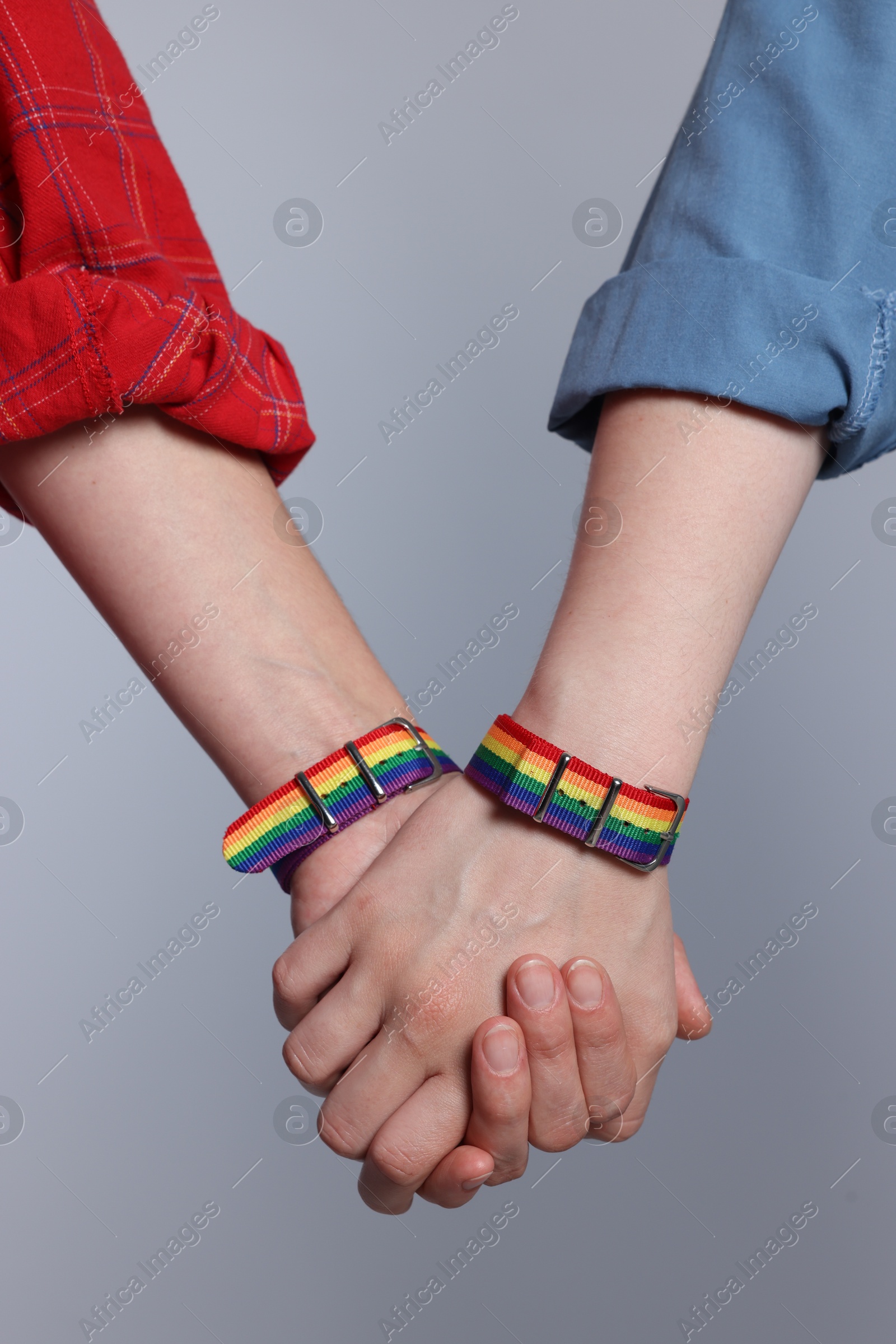 Photo of LGBT concept. Women in rainbow wristbands holding hands on light grey background, closeup