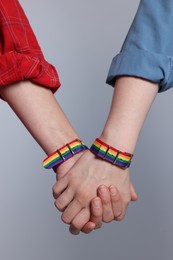 Photo of LGBT concept. Women in rainbow wristbands holding hands on light grey background, closeup