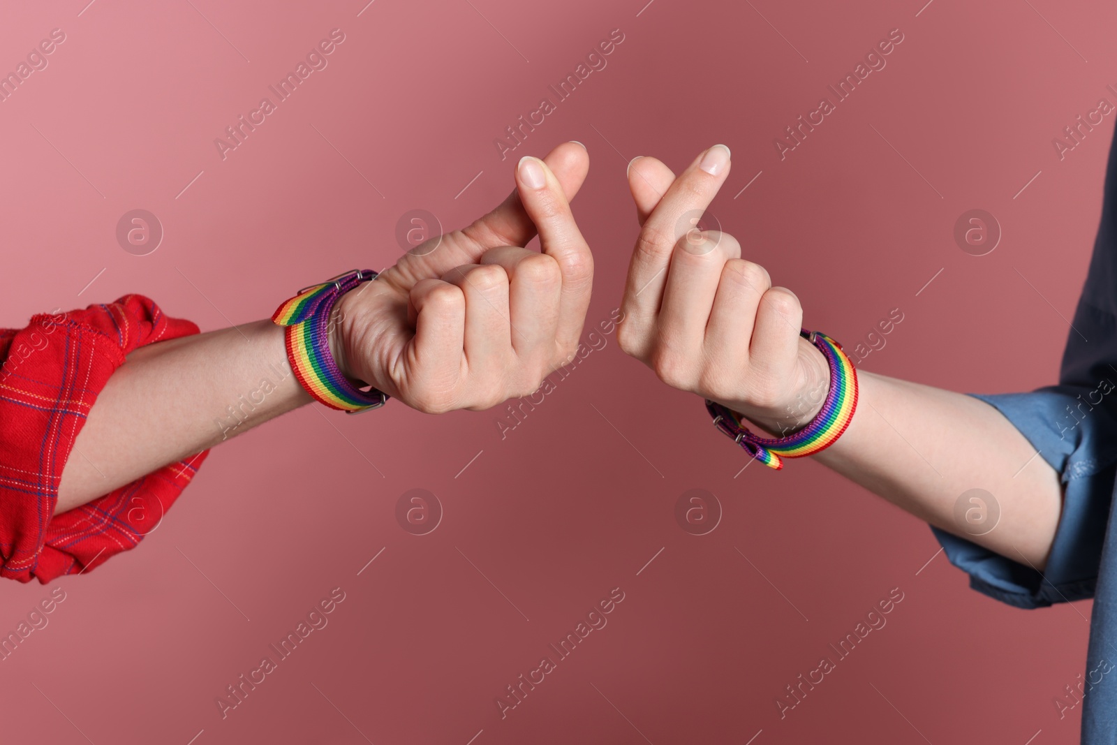 Photo of LGBT concept. Women in rainbow wristbands making heart gestures on pink background, closeup