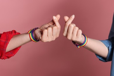 Photo of LGBT concept. Women in rainbow wristbands making heart gestures on pink background, closeup