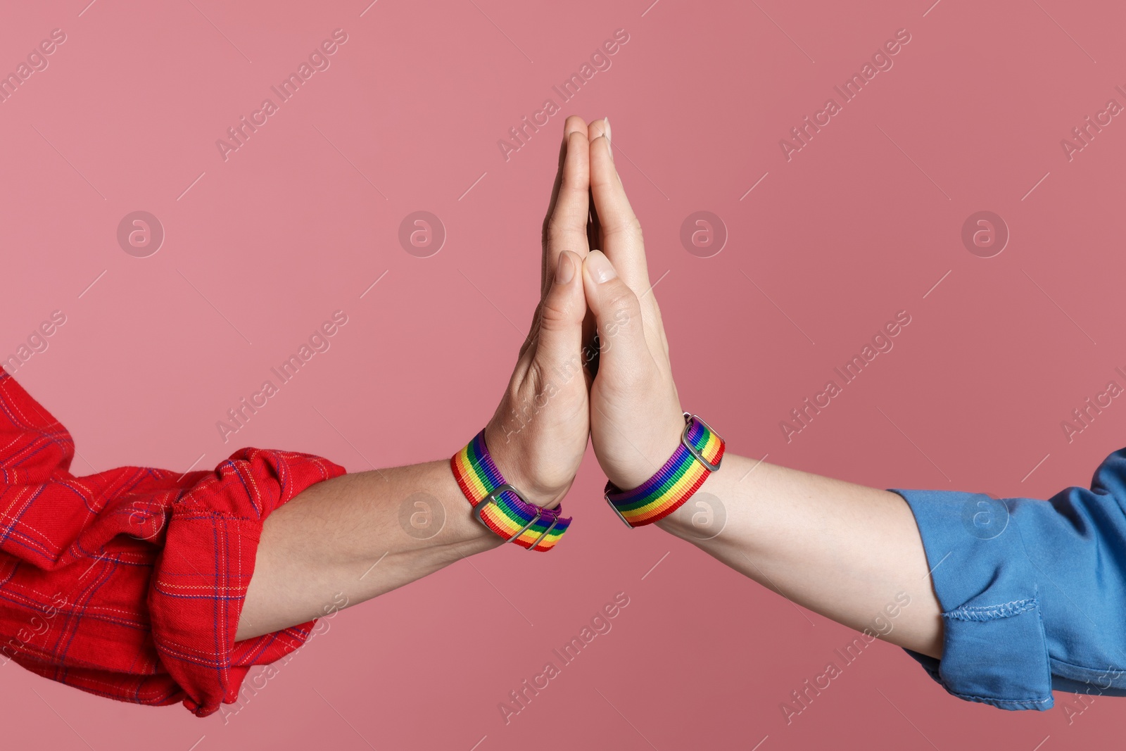 Photo of LGBT concept. Women in rainbow wristbands holding hands on pink background, closeup