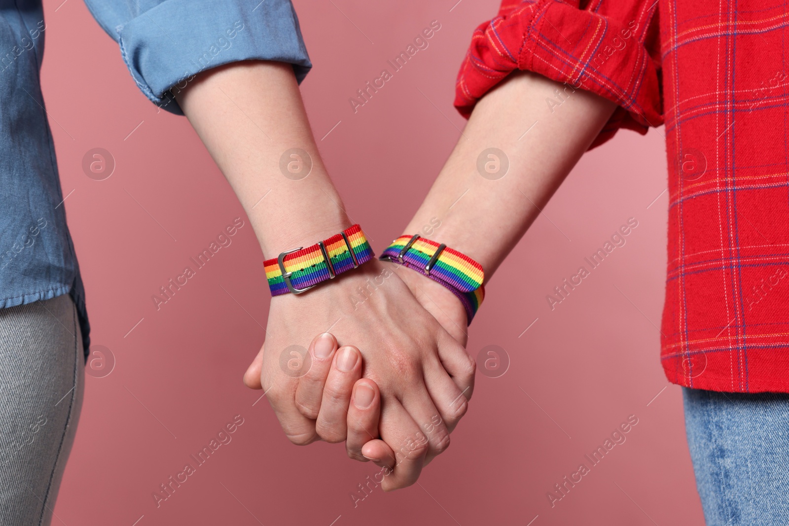 Photo of LGBT concept. Women in rainbow wristbands holding hands on pink background, closeup