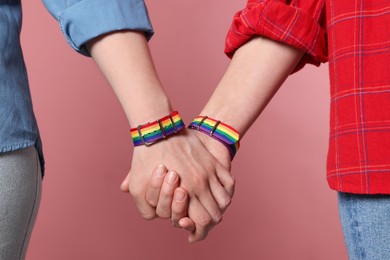 Photo of LGBT concept. Women in rainbow wristbands holding hands on pink background, closeup