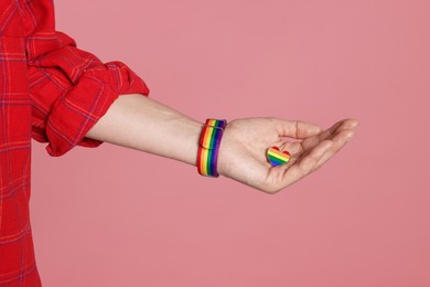 Photo of LGBT concept. Woman in rainbow wristband with heart shaped pin on pink background, closeup