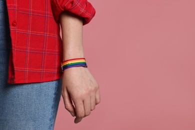 Photo of LGBT concept. Woman in rainbow wristband on pink background, closeup. Space for text