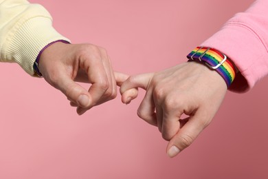 Photo of LGBT concept. Women in rainbow wristbands holding hands on pink background, closeup