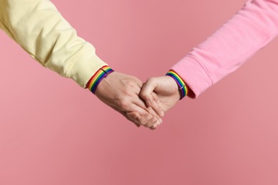 Photo of LGBT concept. Women in rainbow wristbands holding hands on pink background, closeup