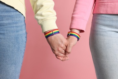 Photo of LGBT concept. Women in rainbow wristbands holding hands on pink background, closeup
