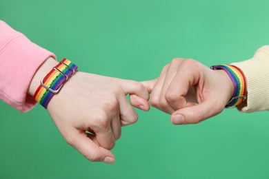 Photo of LGBT concept. Women in rainbow wristbands holding hands on green background, closeup