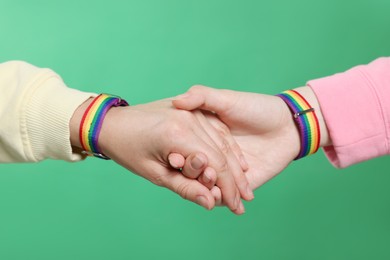 Photo of LGBT concept. Women in rainbow wristbands holding hands on green background, closeup