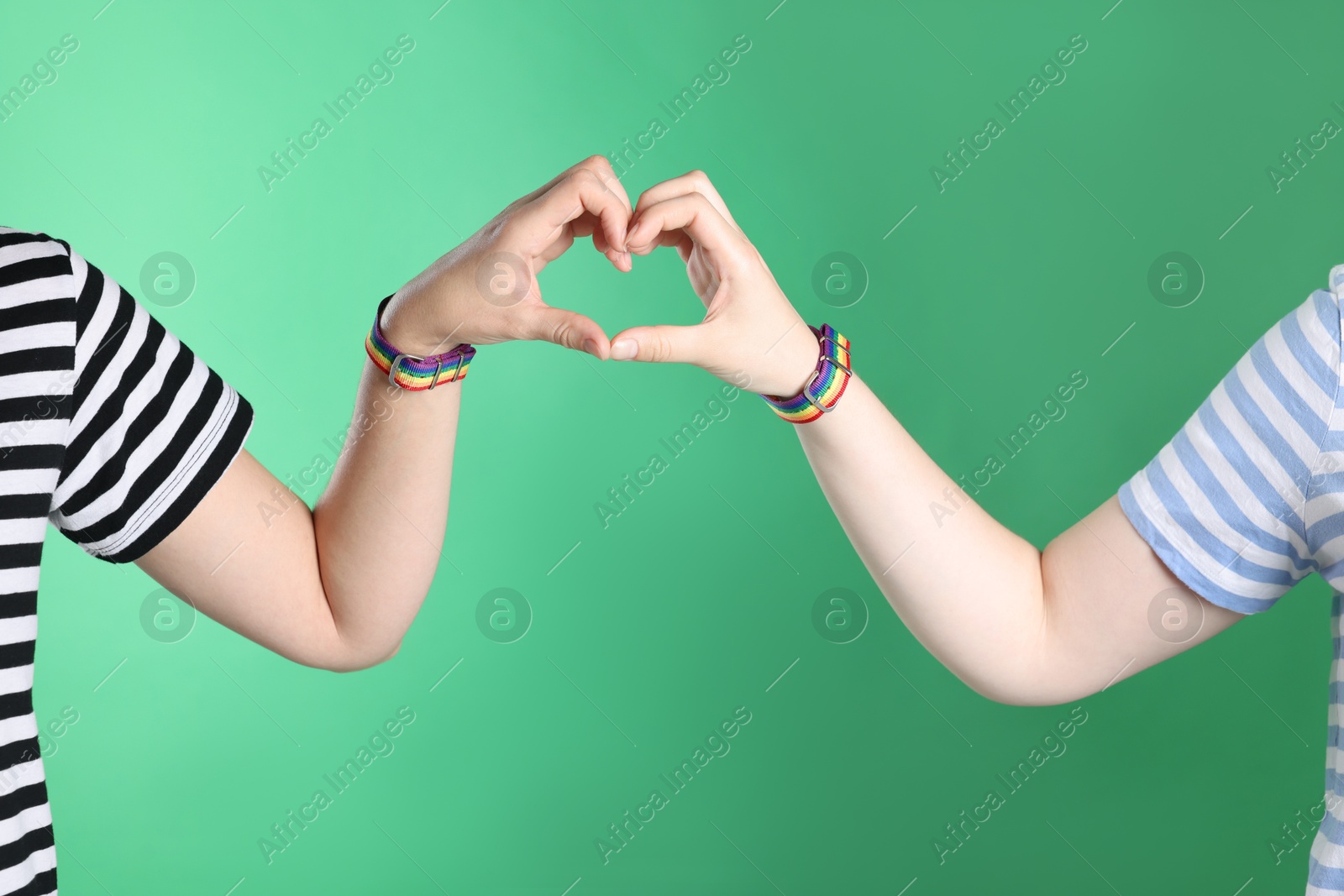 LGBT concept. Women in rainbow wristbands making heart shape on green background, closeup Photo of LGBT concept. Women in rainbow wristbands making heart shape on green background, closeup