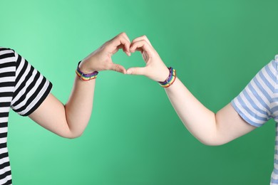 Photo of LGBT concept. Women in rainbow wristbands making heart shape on green background, closeup