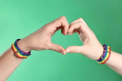 Photo of LGBT concept. Women in rainbow wristbands making heart shape on green background, closeup