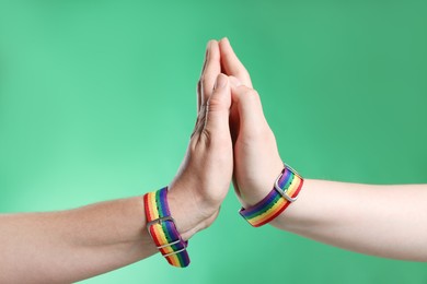 Photo of LGBT concept. Women in rainbow wristbands holding hands on green background, closeup