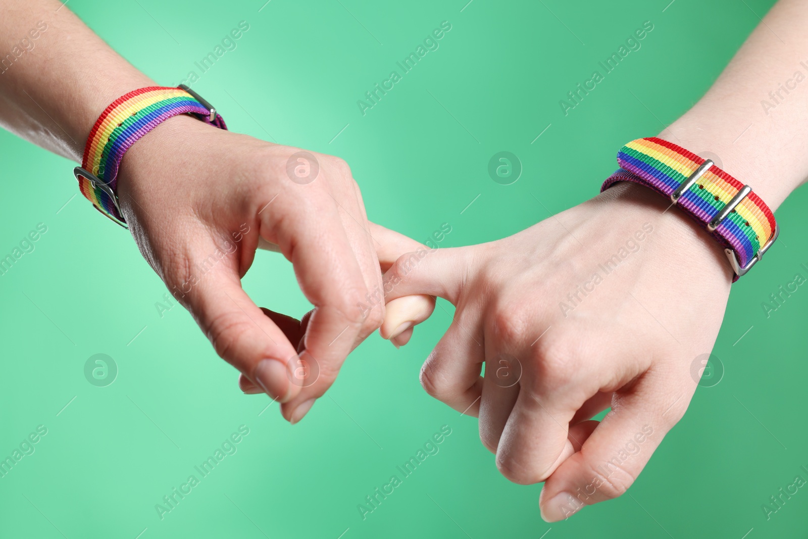 Photo of LGBT concept. Women in rainbow wristbands holding hands on green background, closeup