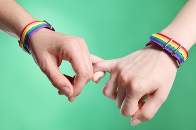 Photo of LGBT concept. Women in rainbow wristbands holding hands on green background, closeup