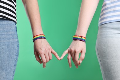 Photo of LGBT concept. Women in rainbow wristbands holding hands on green background, closeup