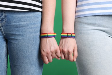 Photo of LGBT concept. Women in rainbow wristbands holding hands on green background, closeup