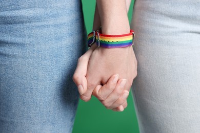 Photo of LGBT concept. Women in rainbow wristbands holding hands on green background, closeup