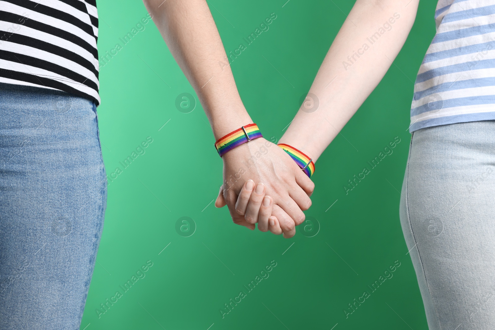 Photo of LGBT concept. Women in rainbow wristbands holding hands on green background, closeup