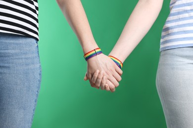 Photo of LGBT concept. Women in rainbow wristbands holding hands on green background, closeup