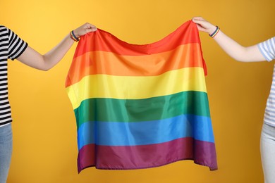 Photo of LGBT concept. Women in rainbow wristbands with flag on yellow background, closeup