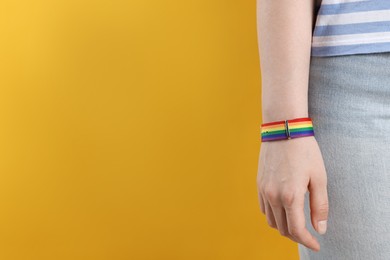 Photo of LGBT concept. Woman in rainbow wristband on yellow background, closeup. Space for text