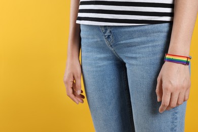 Photo of LGBT concept. Woman in rainbow wristband on yellow background, closeup