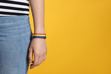 Photo of LGBT concept. Woman in rainbow wristband on yellow background, closeup. Space for text
