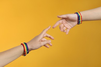 Photo of LGBT concept. Women in rainbow wristbands on yellow background, closeup