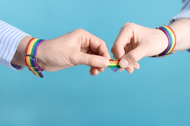 Photo of LGBT concept. Women in rainbow wristbands with heart shaped pin on light blue background, closeup