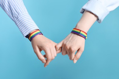 Photo of LGBT concept. Women in rainbow wristbands holding hands on light blue background, closeup