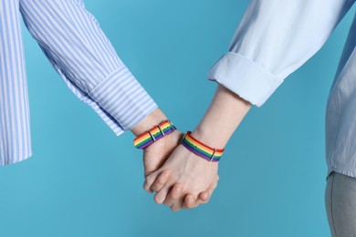 Photo of LGBT concept. Women in rainbow wristbands holding hands on light blue background, closeup