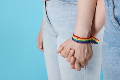 Photo of LGBT concept. Women in rainbow wristbands holding hands on light blue background, closeup. Space for text
