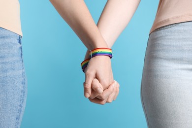 Photo of LGBT concept. Women in rainbow wristbands holding hands on light blue background, closeup