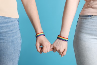 Photo of LGBT concept. Women in rainbow wristbands holding hands on light blue background, closeup