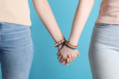 Photo of LGBT concept. Women in rainbow wristbands holding hands on light blue background, closeup