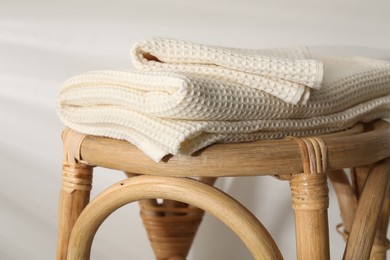 Photo of Folded waffle towels on wicker chair near light wall, closeup