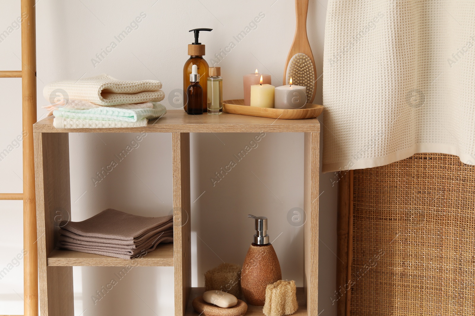 Photo of Clean waffle towels, burning candles and spa products on shelving unit near white wall in bathroom