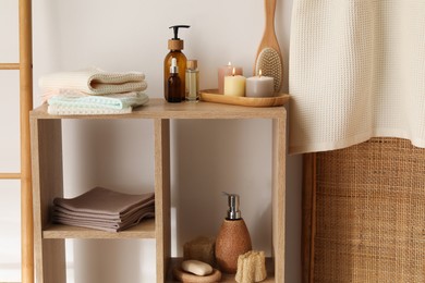 Photo of Clean waffle towels, burning candles and spa products on shelving unit near white wall in bathroom