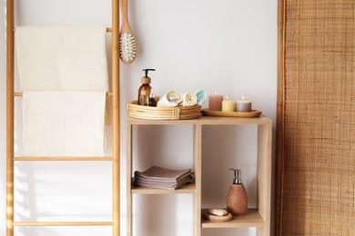 Photo of Clean waffle towels, burning candles and spa products on shelving unit near white wall in bathroom