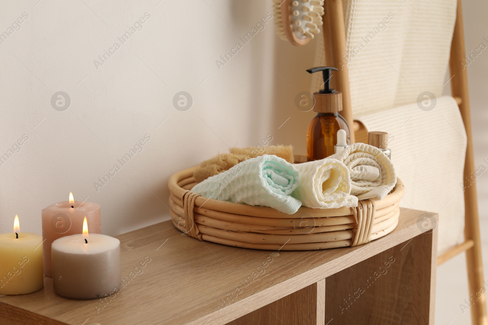 Photo of Clean waffle towels, burning candles and spa products on shelving unit near white wall in bathroom