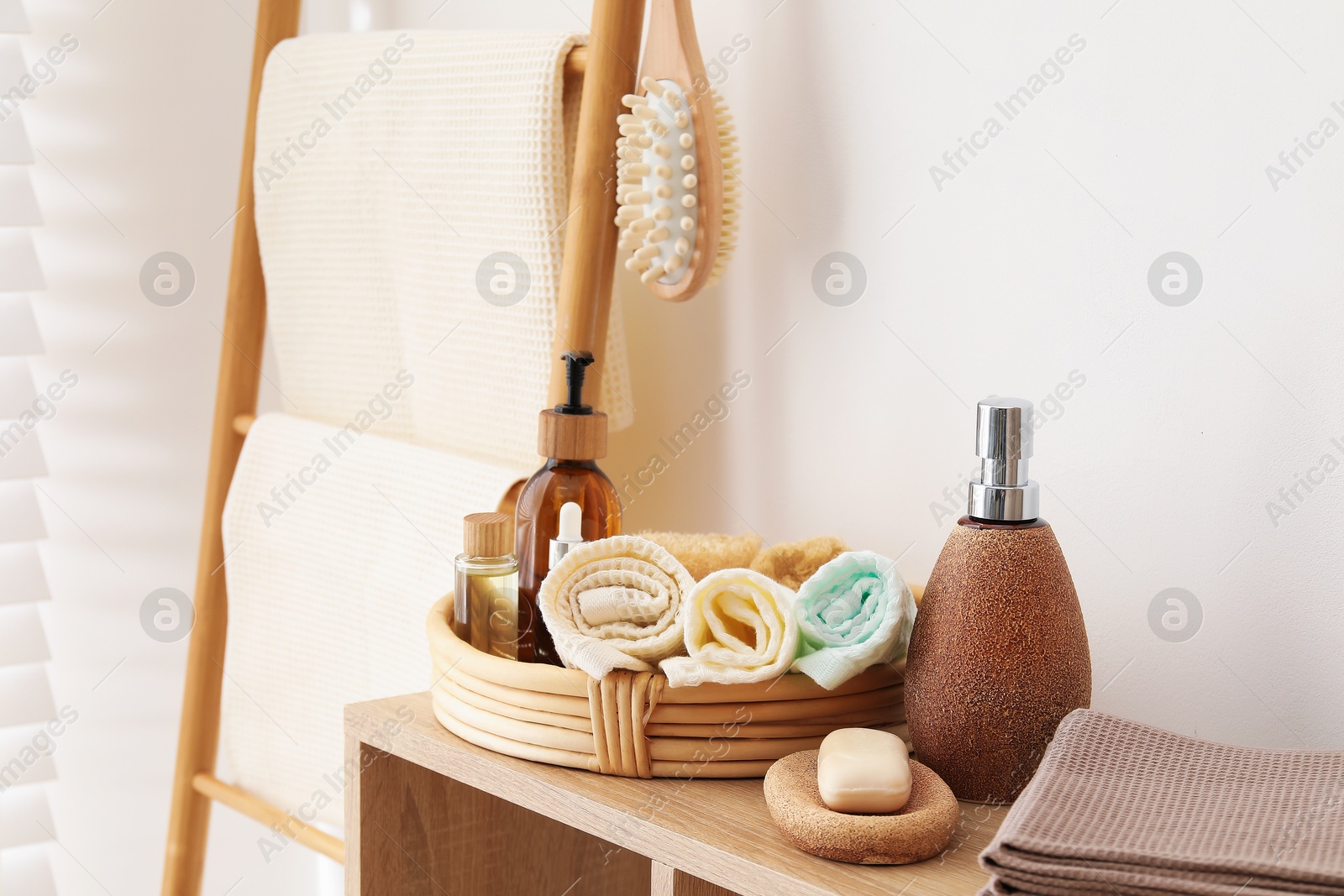 Photo of Clean waffle towels and spa products on shelving unit near white wall in bathroom